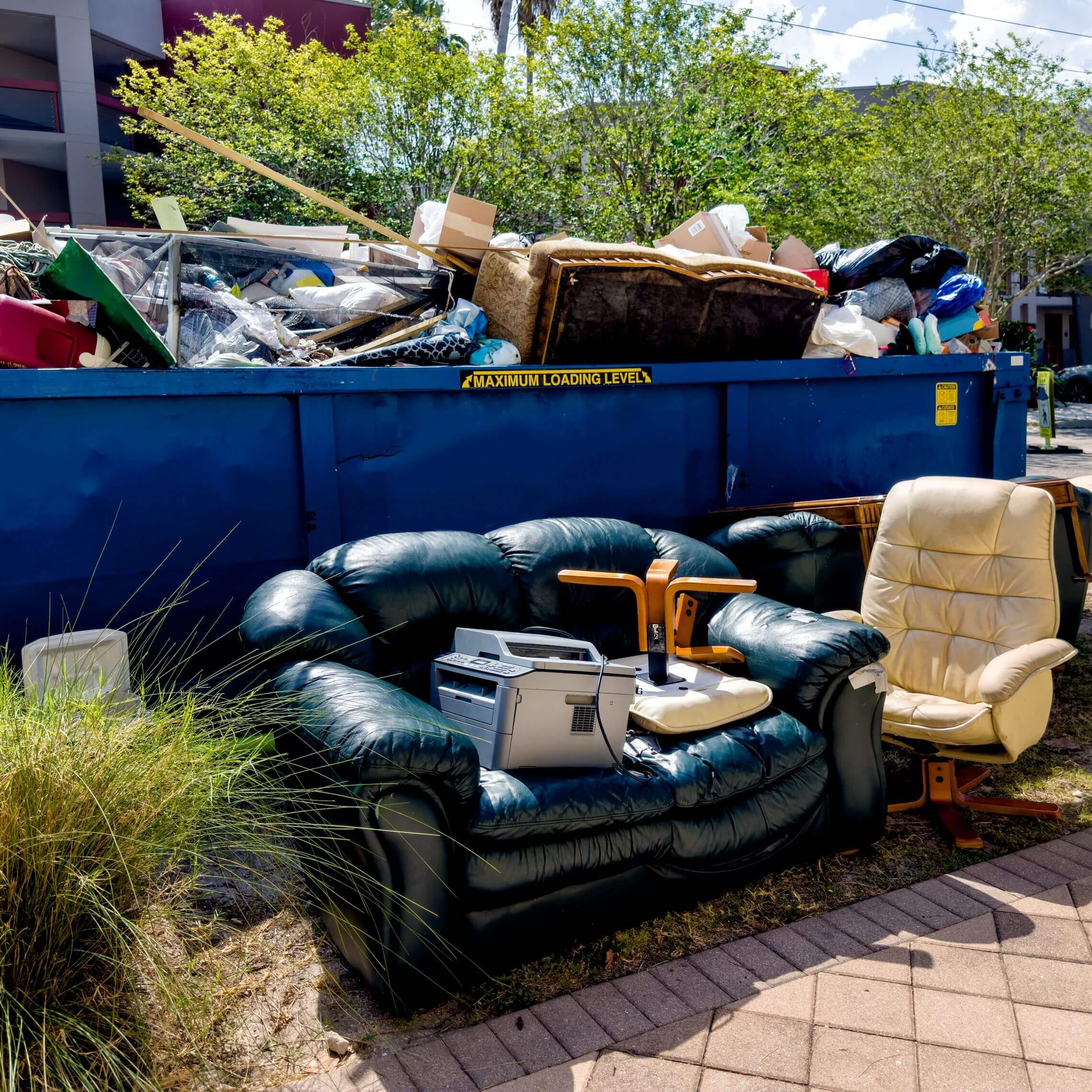 Discarded furniture and trash in front of dumpster.