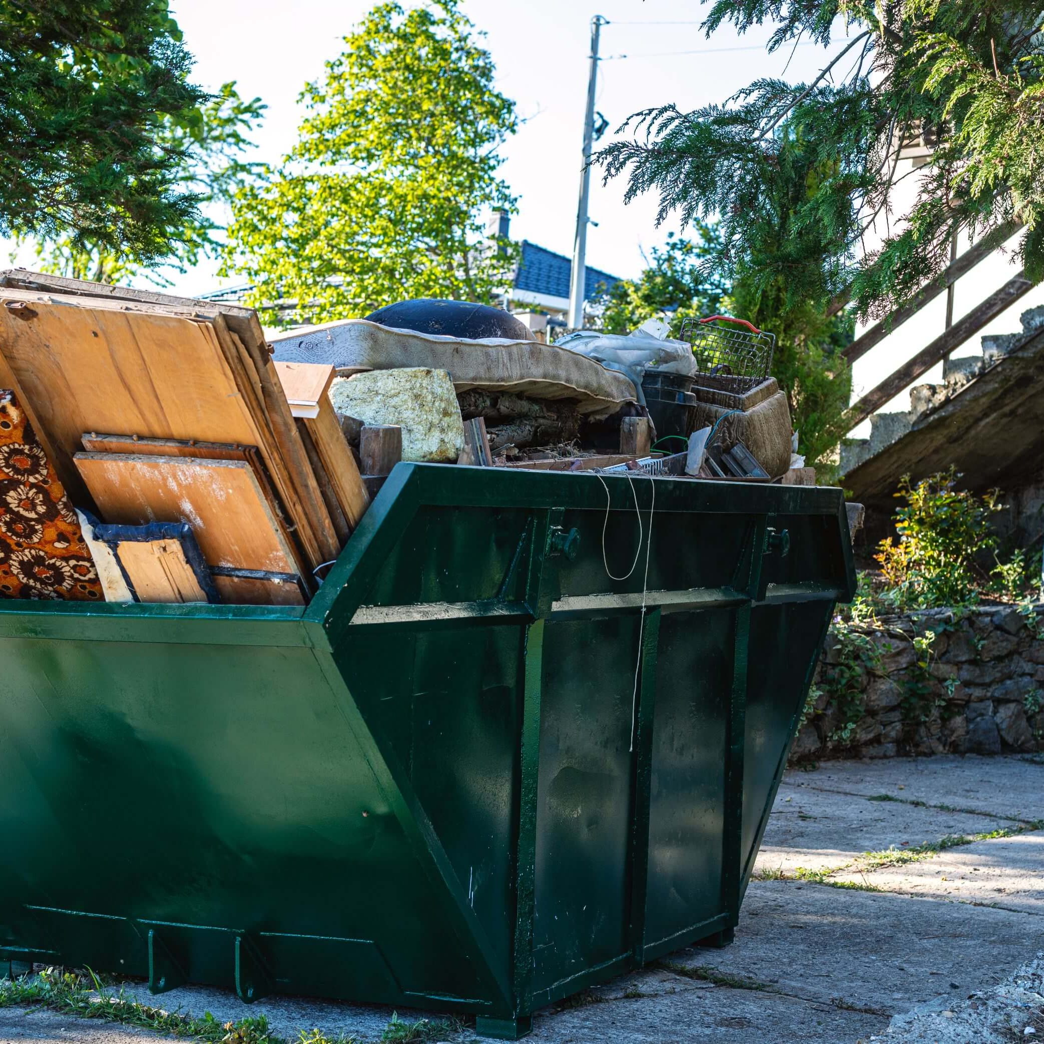 Green dumpster filled with wooden debris outside.