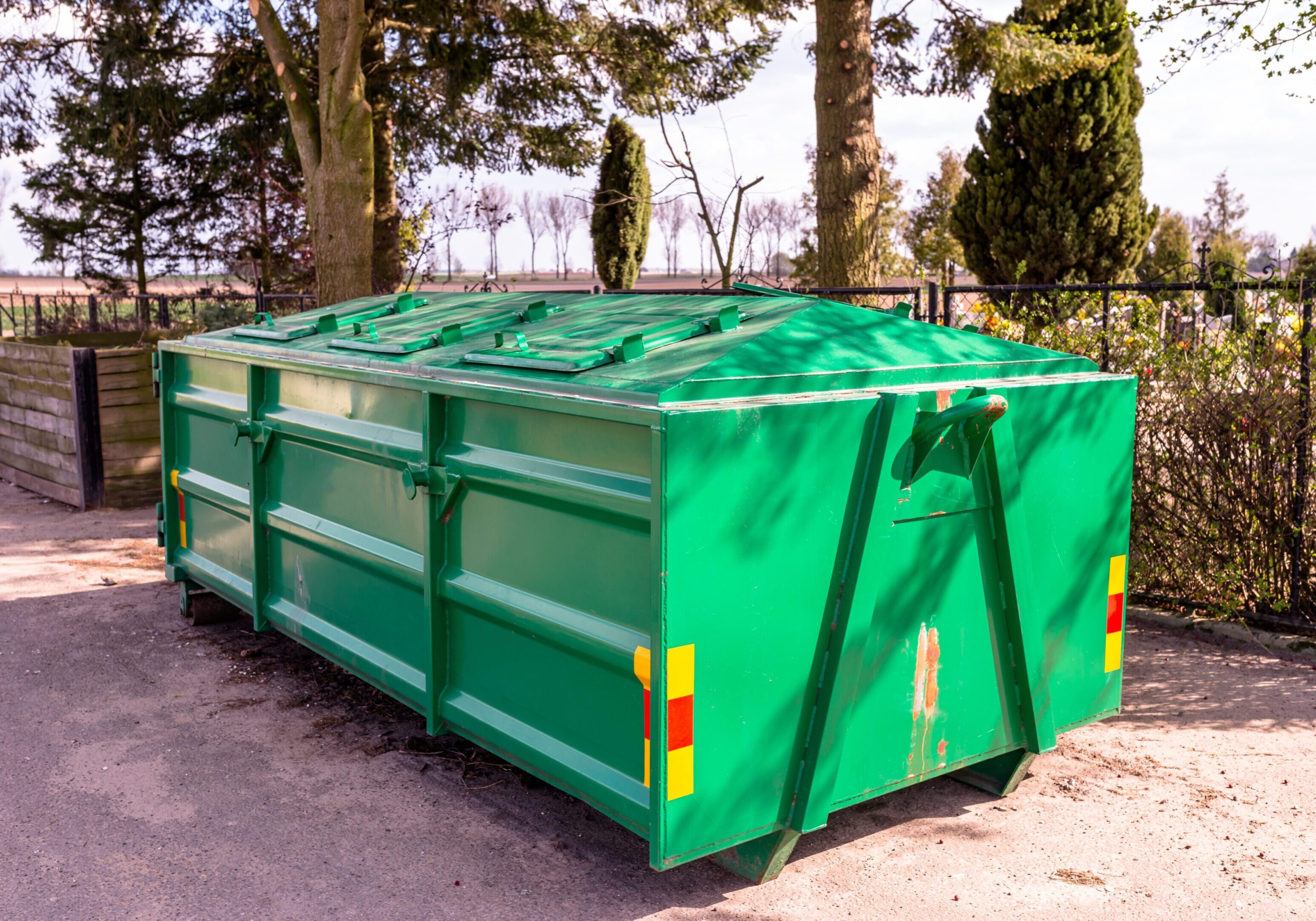 A Large, Metal, Green Garbage Container And Municipal Waste, Standing On A Dirt Road Near The Fence Photo taken in Bydgoszcz, Poland