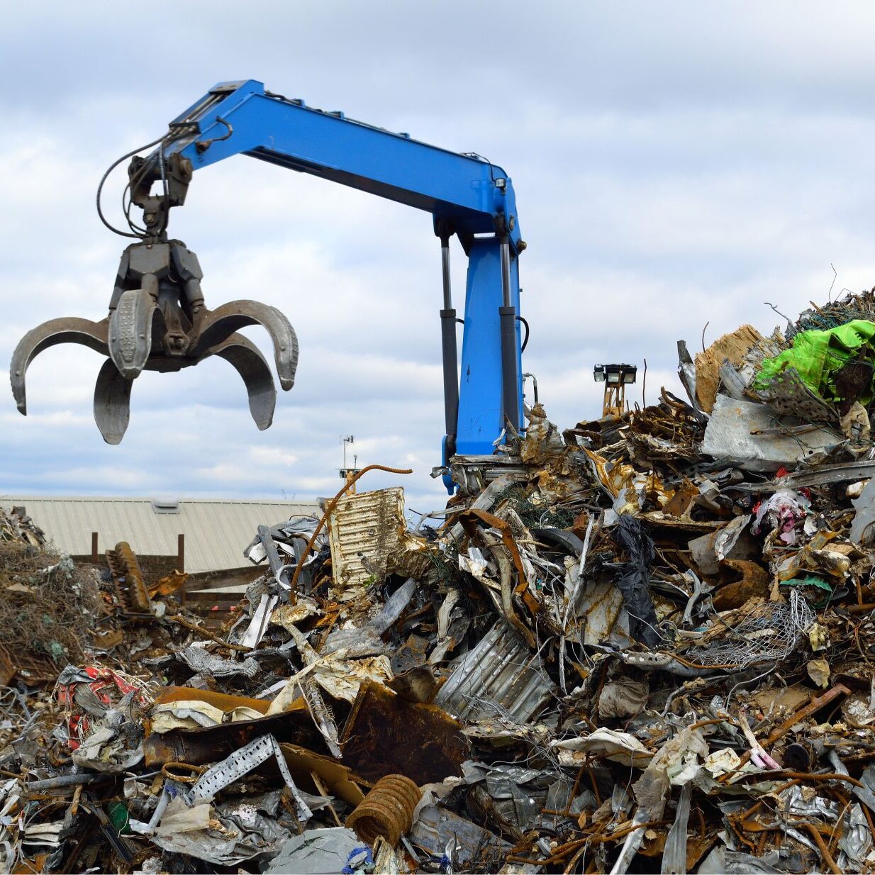 Crane claw sorting through metal scrap pile.